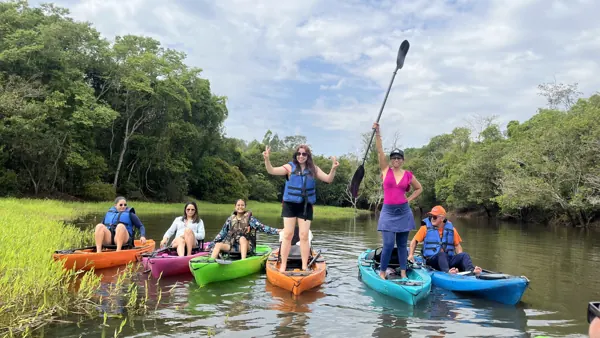 Grupo em caiaques coloridos no rio, de dia, comemorando com o remo para cima