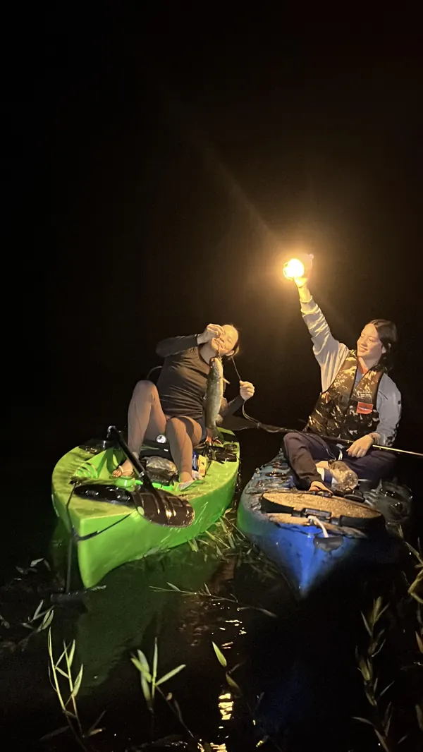 Duas pessoas em caiaques à noite, uma levantando a lanterna
